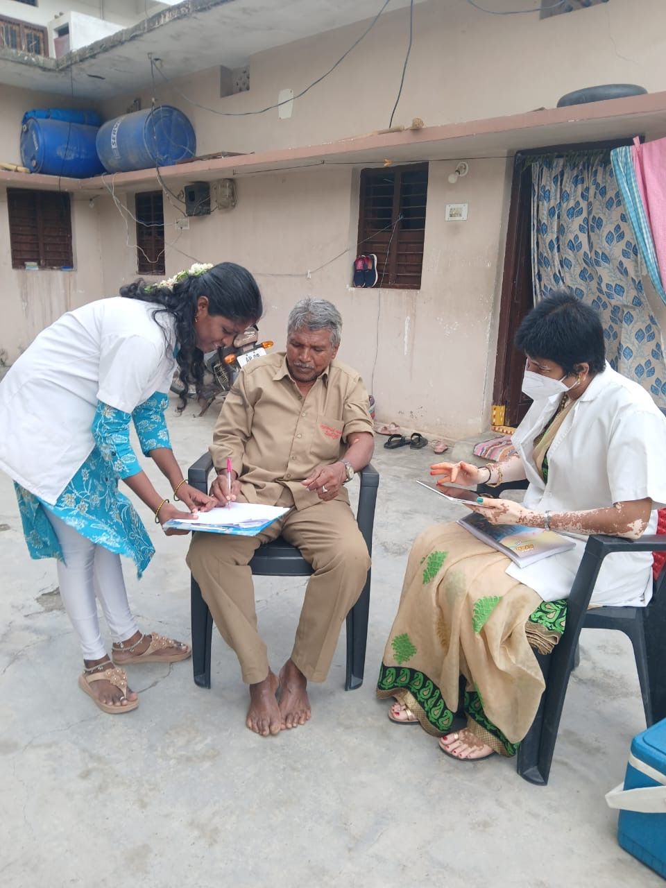Two health workers talking with an old man and filling out a form