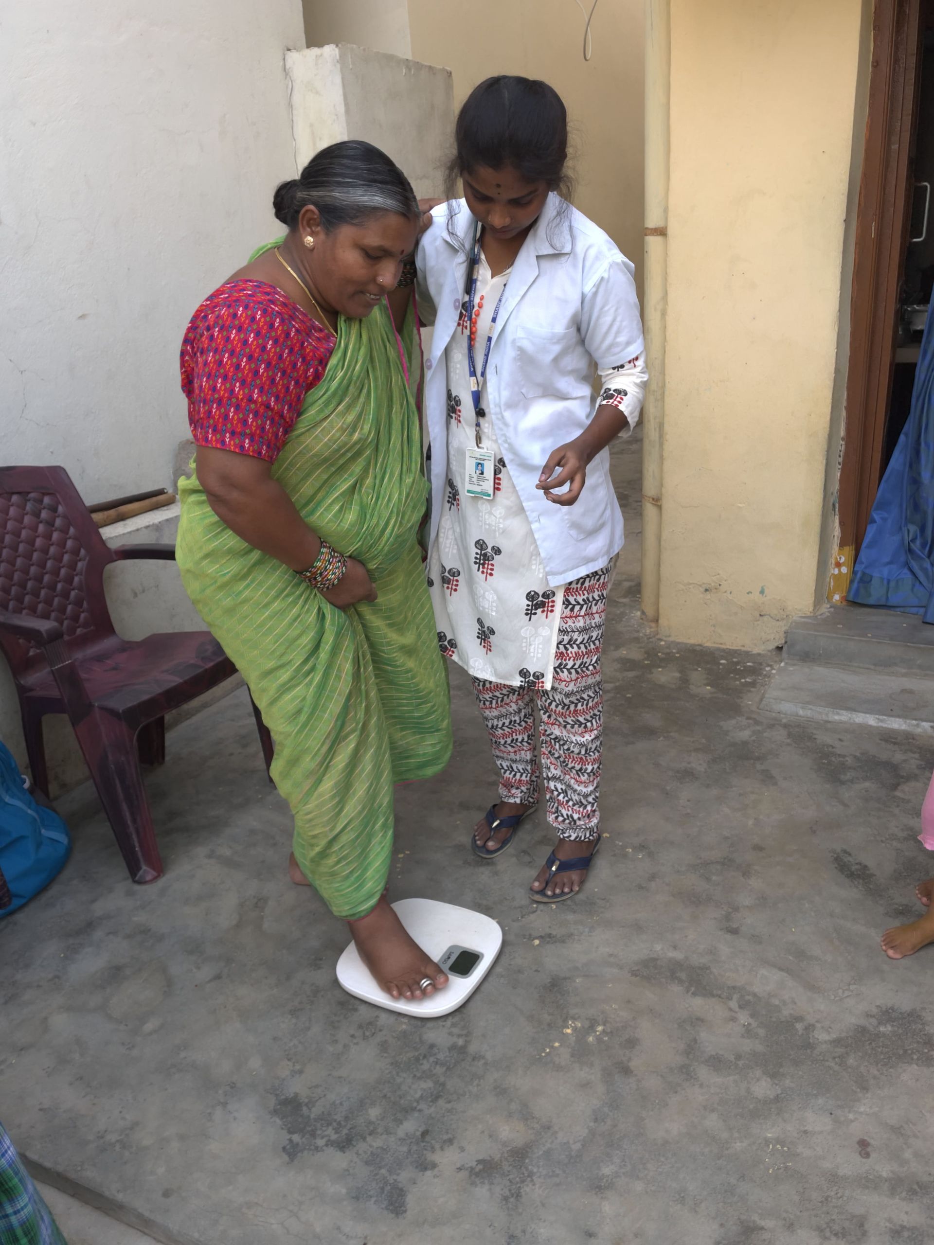 Healthcare worker measuring woman’s weight using digital scale during home visit