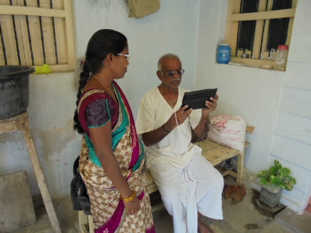 An old man looking at a tablet screen while a health instructor guides him