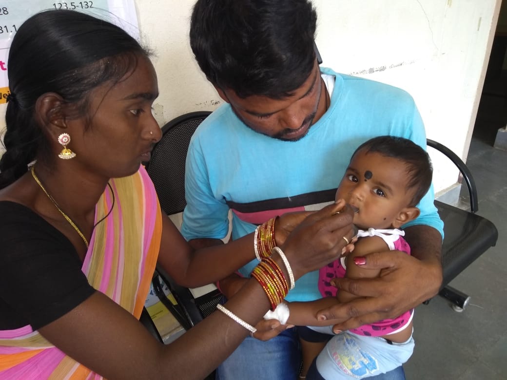 Healthcare worker administering oral vaccine to infant while parent holds child