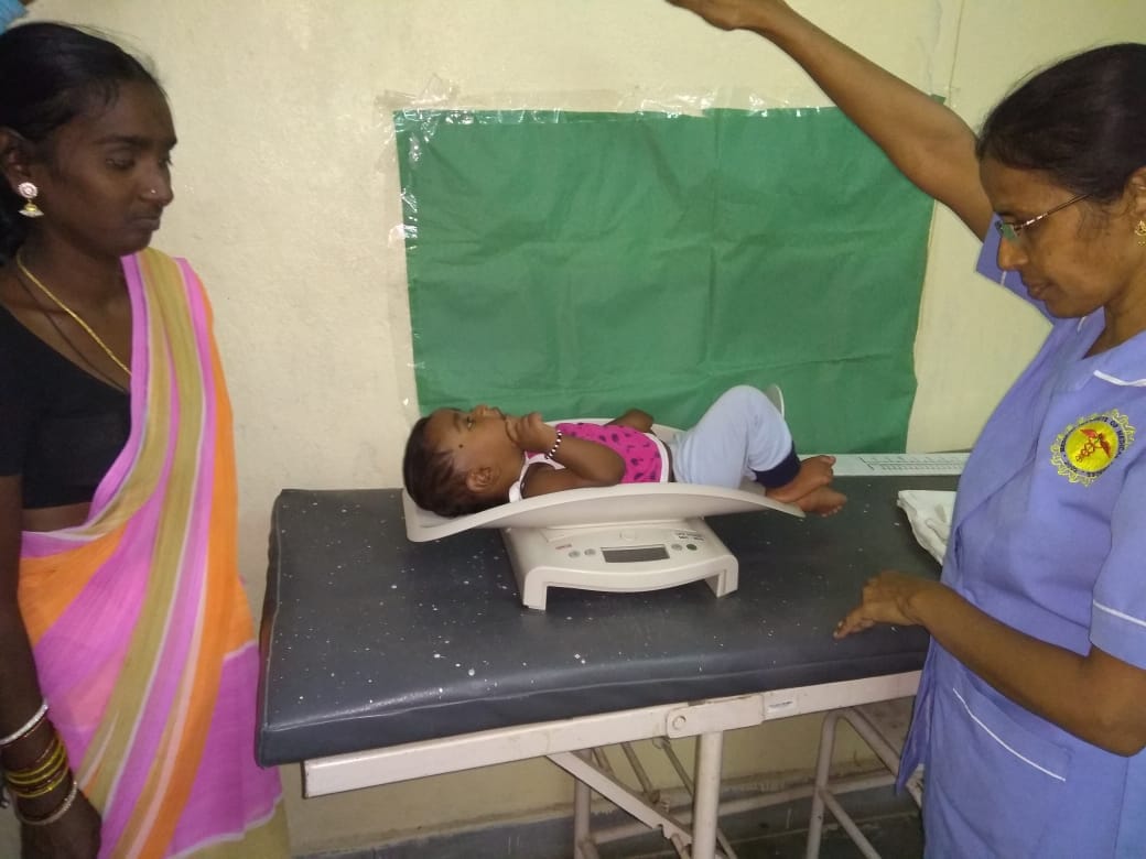 Infant being weighed on digital scale by healthcare worker with mother present