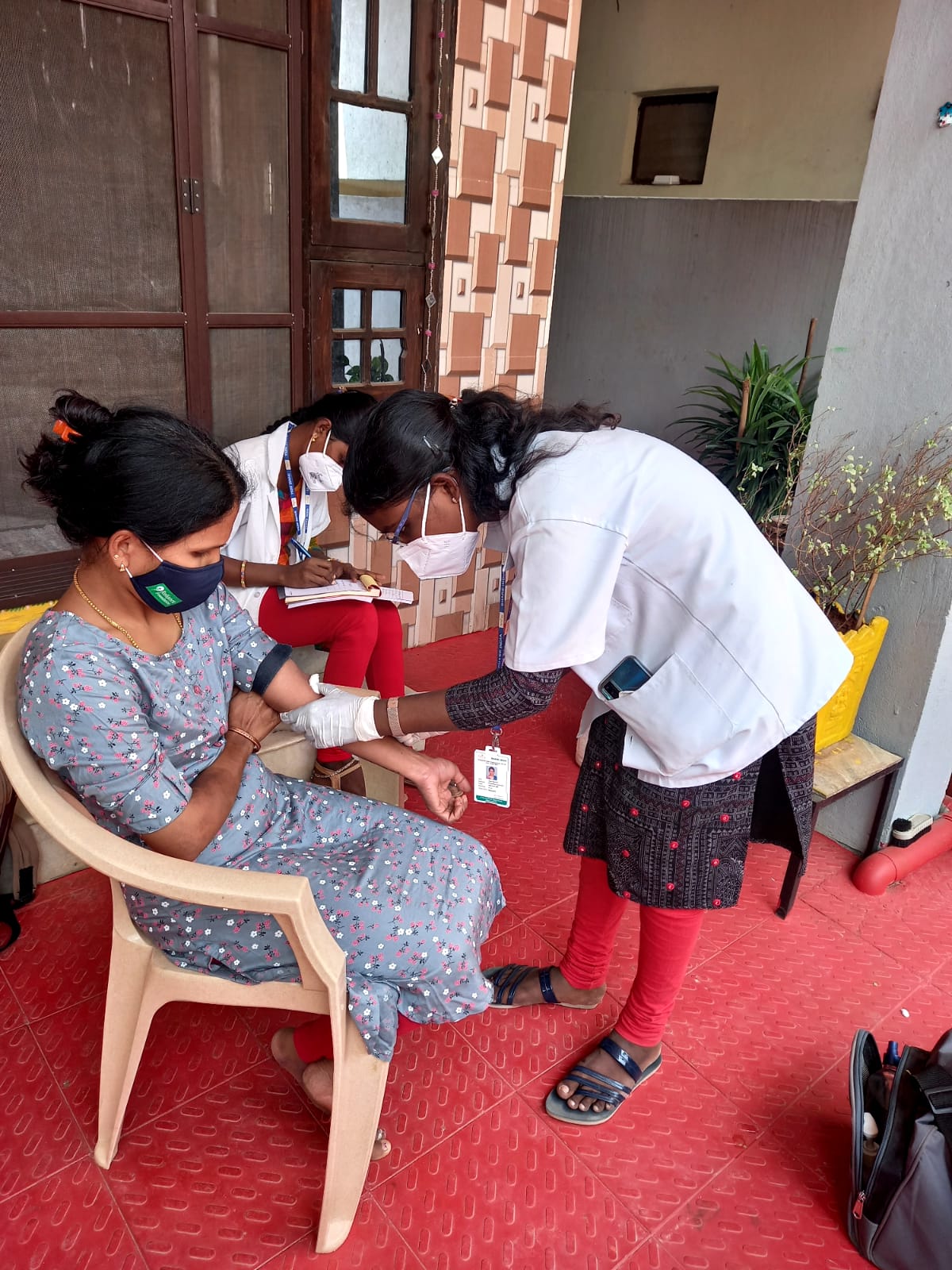 Healthcare worker collecting blood sample from woman during home visit