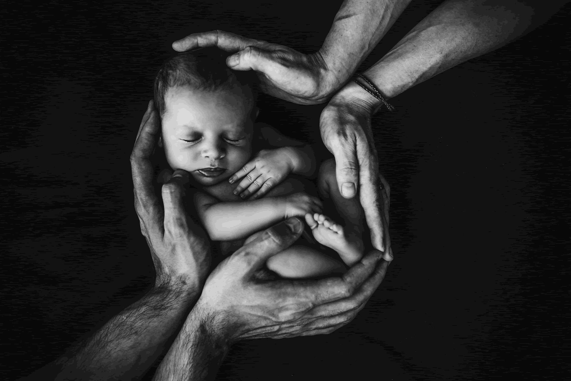 Newborn baby gently held in protective hands on dark background