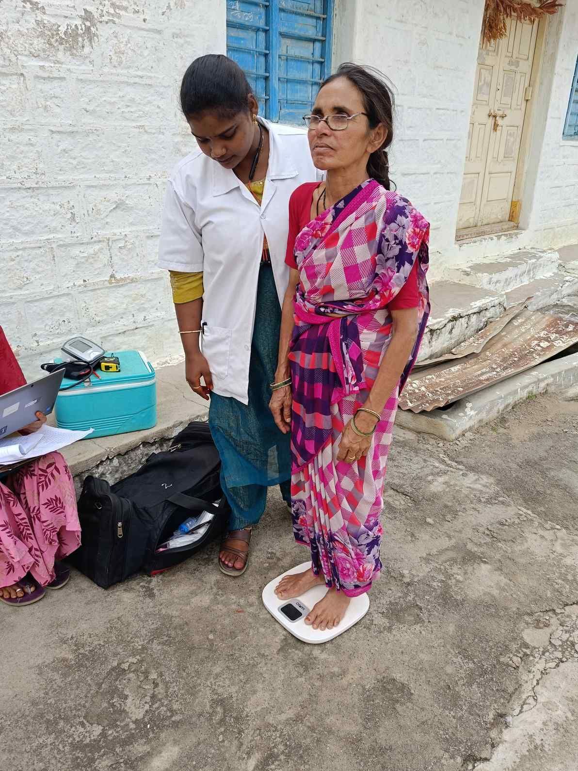 A health worker measuring the weight of a lady on a weighing machine.