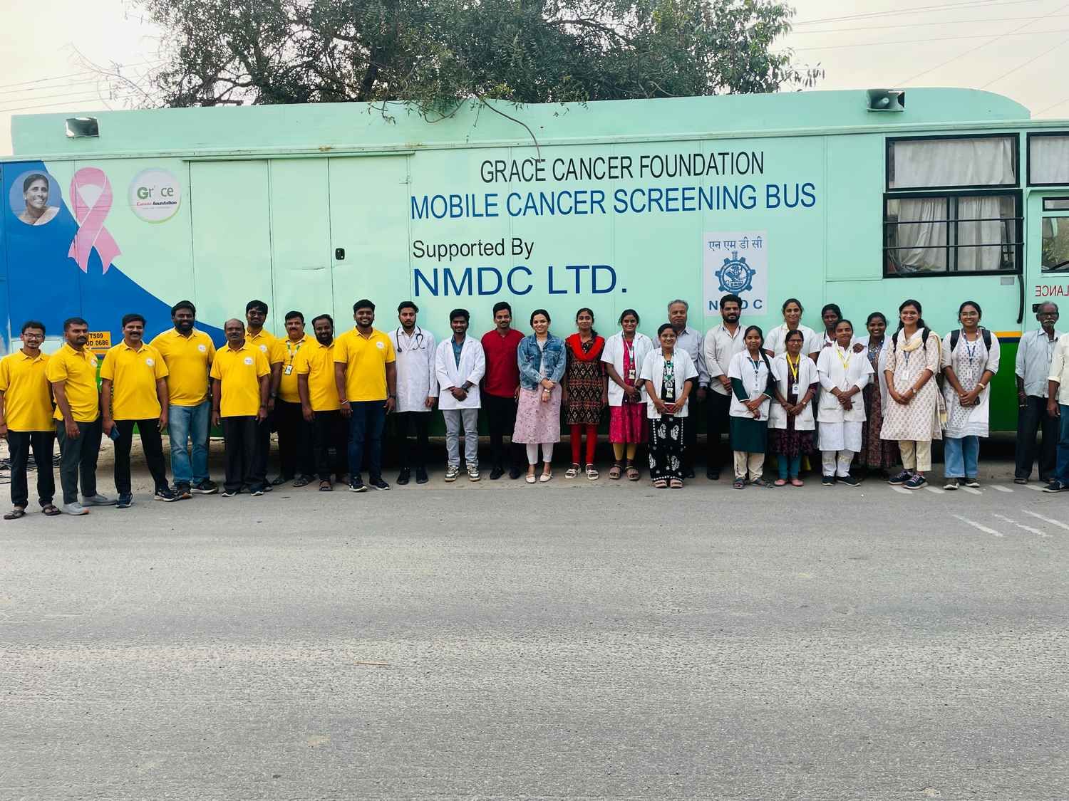 Team of healthcare professionals and volunteers standing in front of a mobile cancer screening bus during a community health initiative