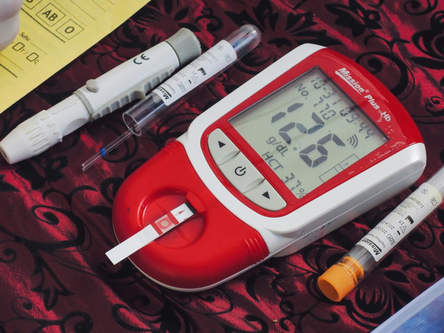 A portable hemoglobin testing device showing blood levels alongside lancets and sample tubes.