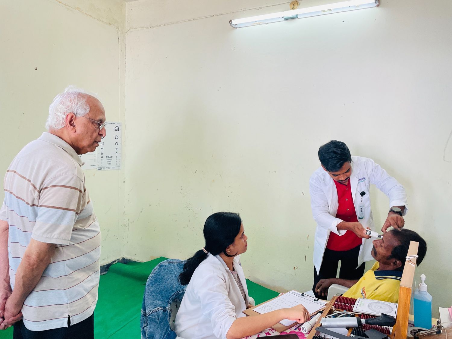 Dr. P.S. Reddy (left) observing a clinical eye examination being conducted by healthcare professionals during a medical screening session