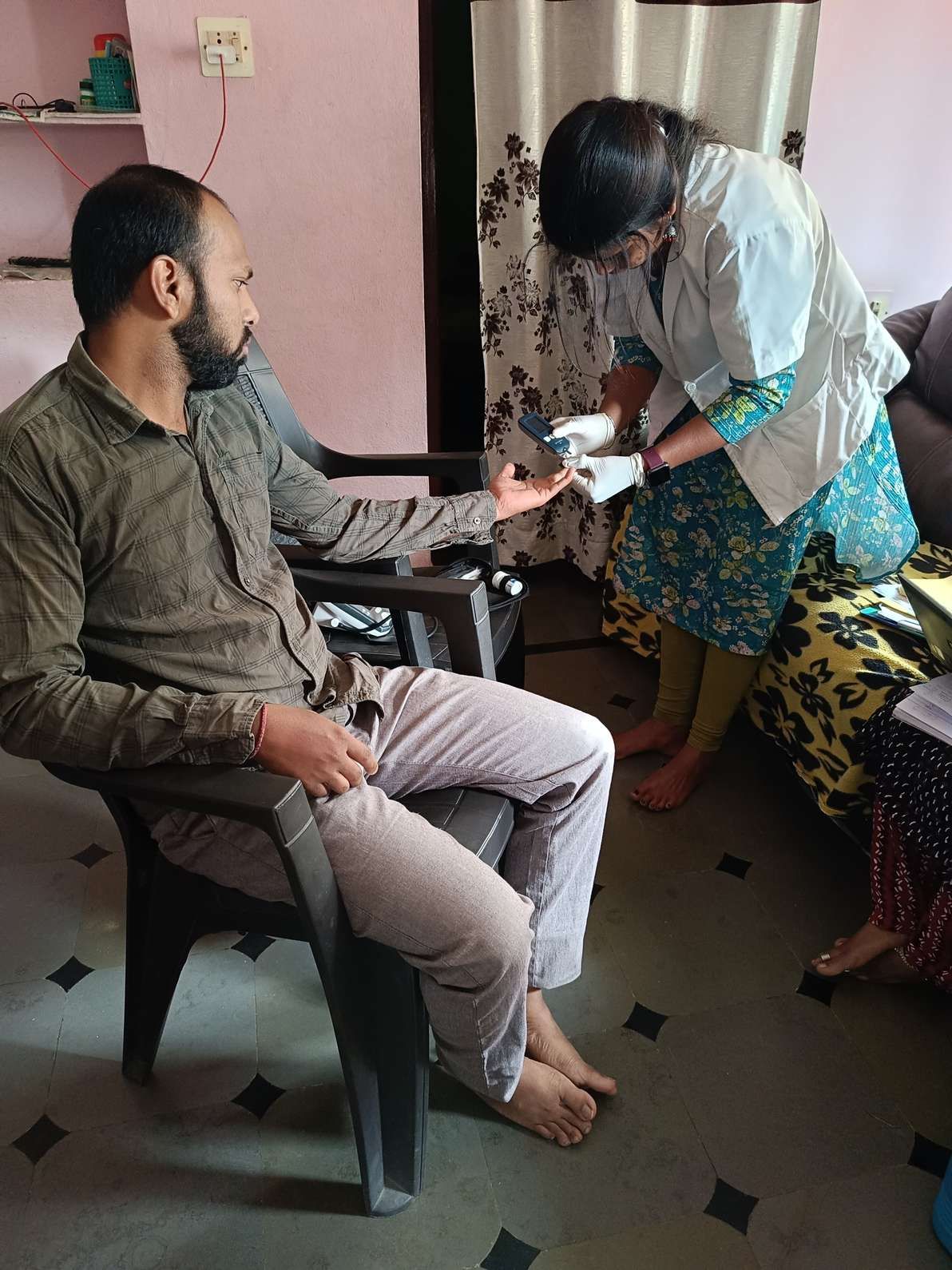 Healthcare worker performing a finger-prick blood glucose test for a patient during a home visit