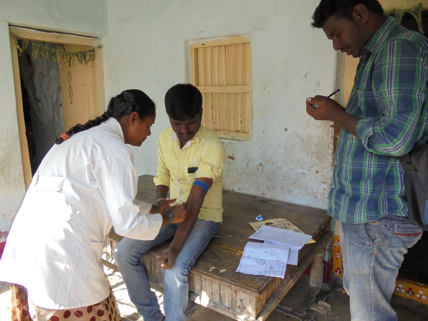 Healthcare worker collecting blood sample from man while colleague records data
