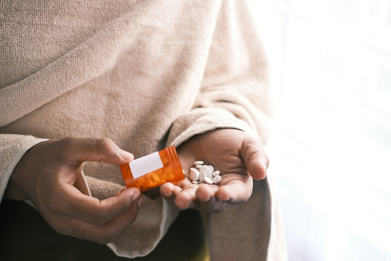 Man's hand with pills spilled out of the container.
