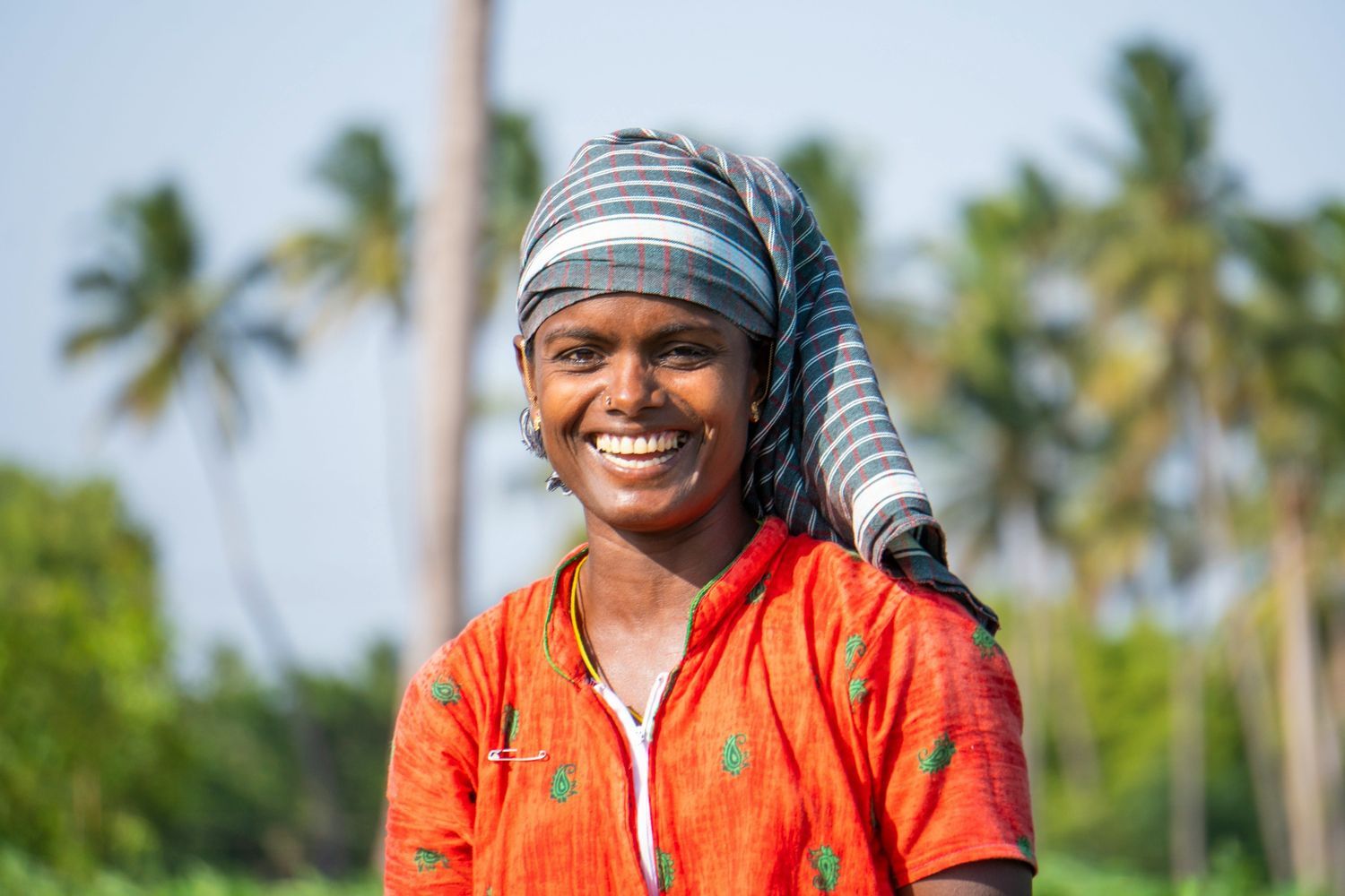 A smiling rural woman wearing a headscarf standing outdoors