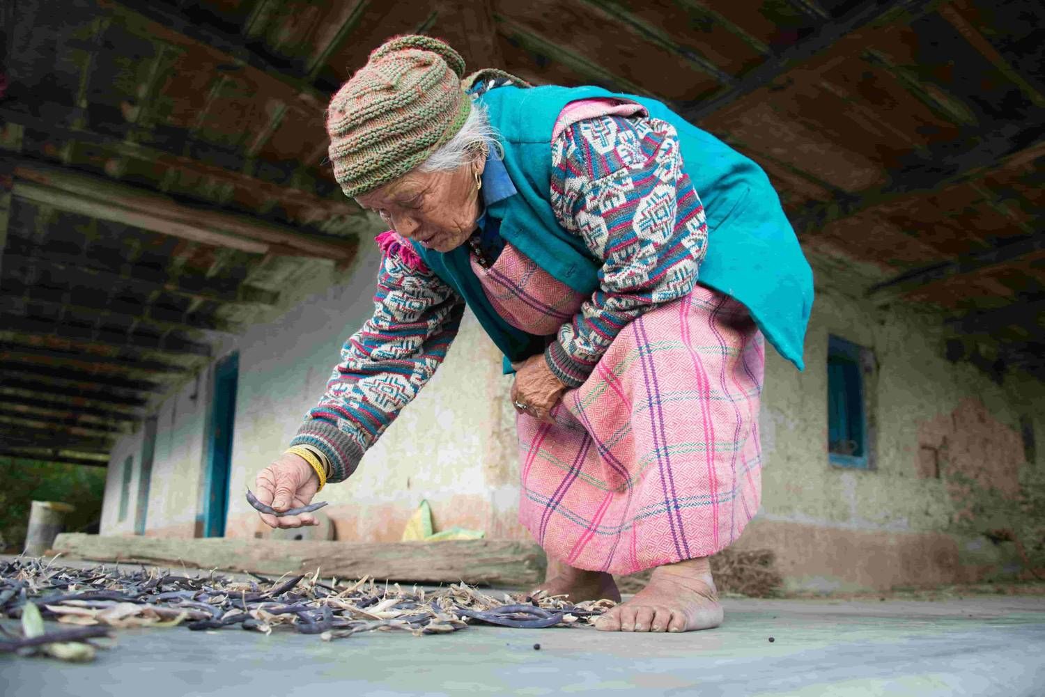 An elderly woman carefully sorting or picking items while working on the ground outside her home.