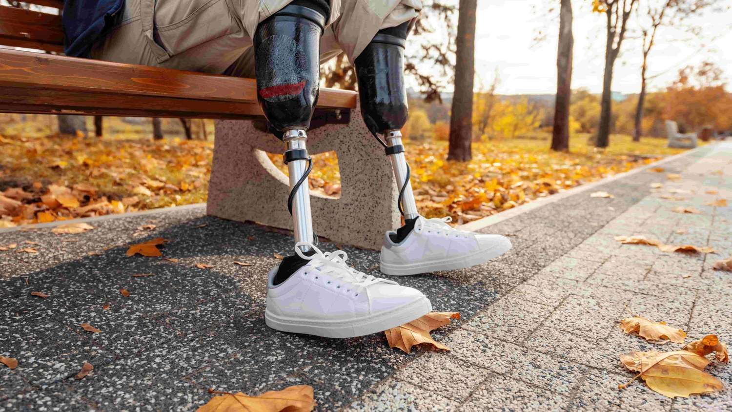 View of a man with prosthetic legs and white sneakers sitting on a bench in a park