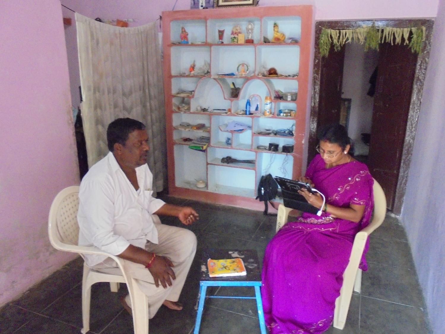 Community health worker recording patient information during a household visit in a rural home setting