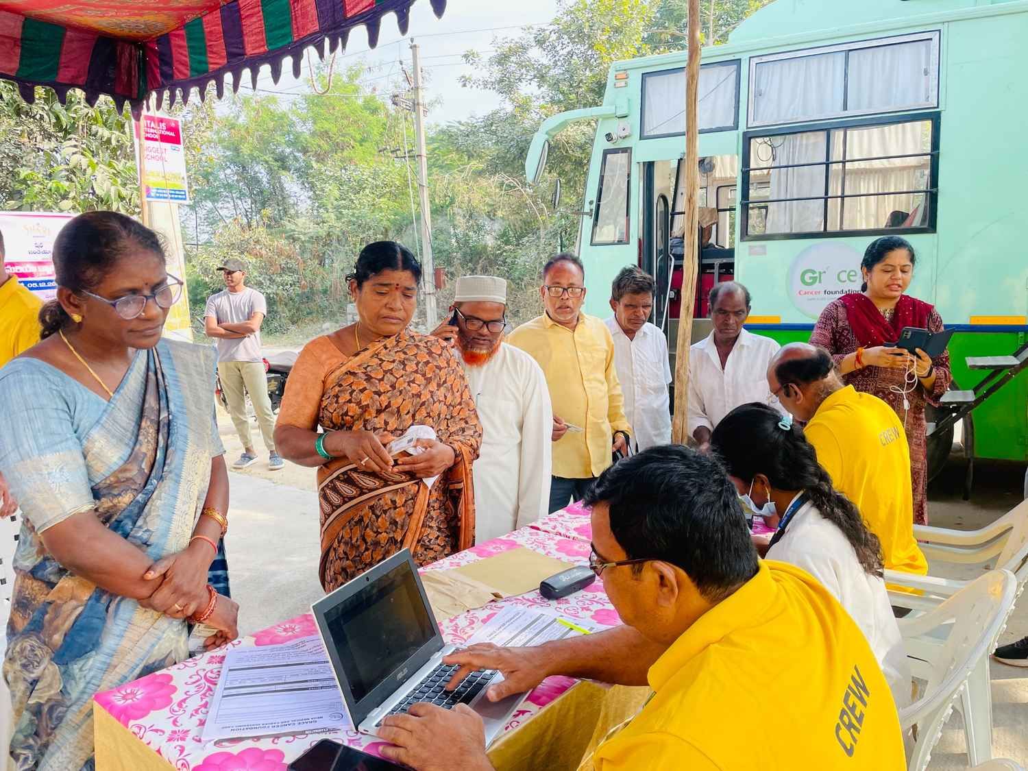 People registering and waiting at a rural mobile health screening camp near a medical bus.