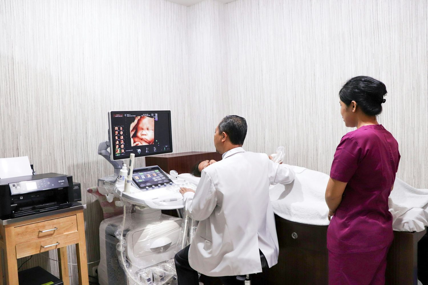 Doctor performing an ultrasound scan to monitor fetal development while a healthcare assistant observes in a clinical setting