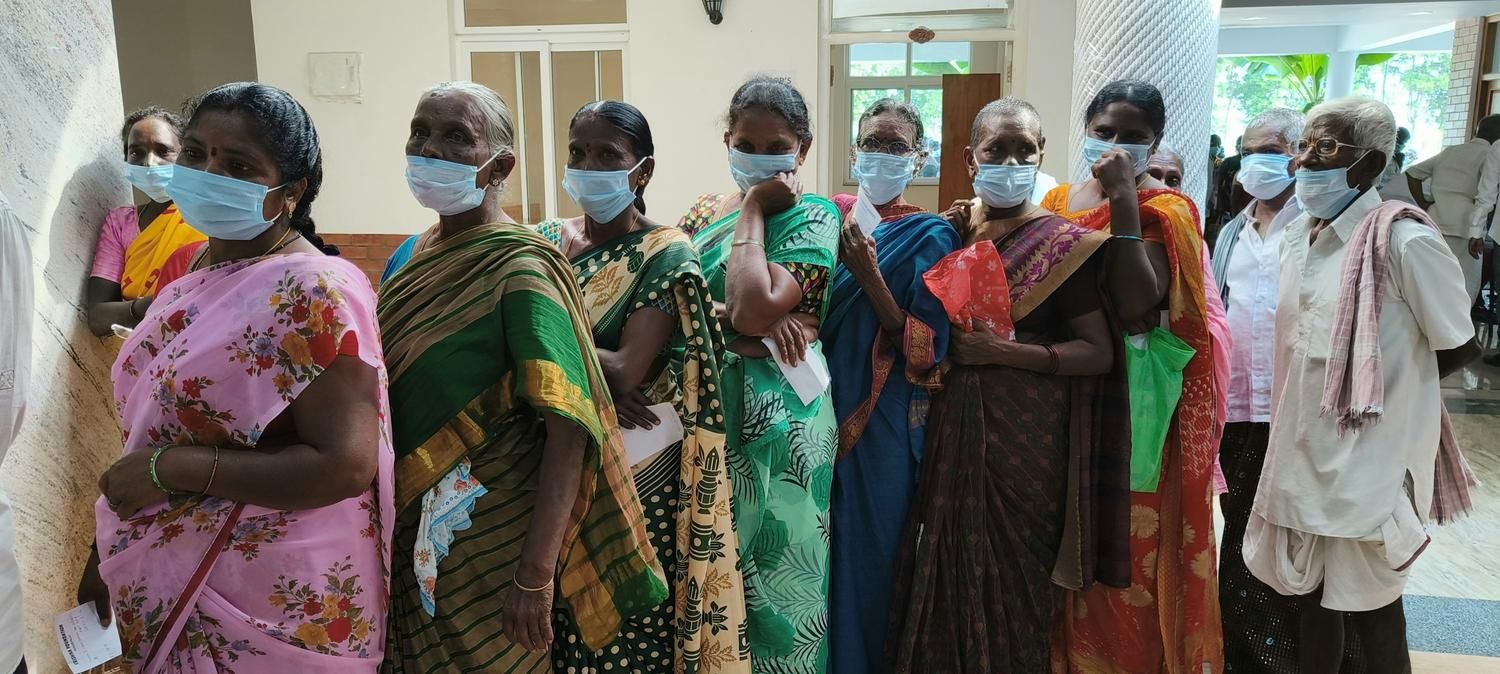 A line of rural patients wearing masks waiting for medical services or screening.