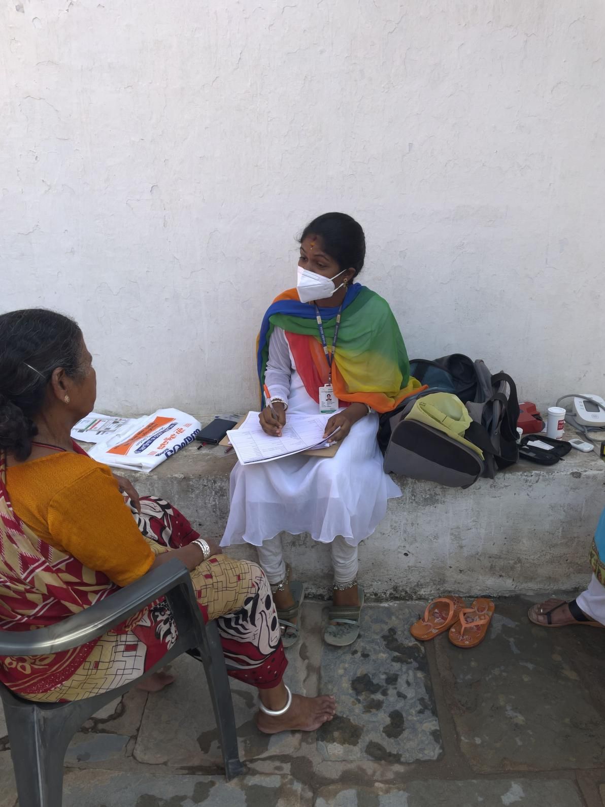 A community health worker in India conducts a medical consultation with an elderly woman outdoors