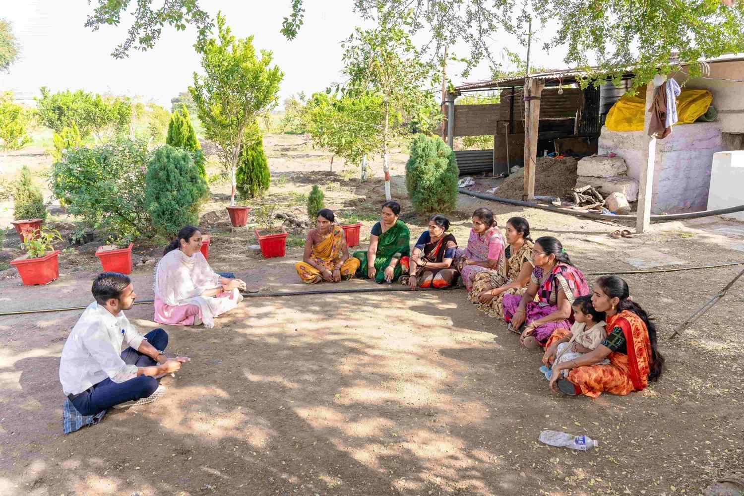 Community health awareness session with women gathered outdoors, participating in group discussion in a rural setting