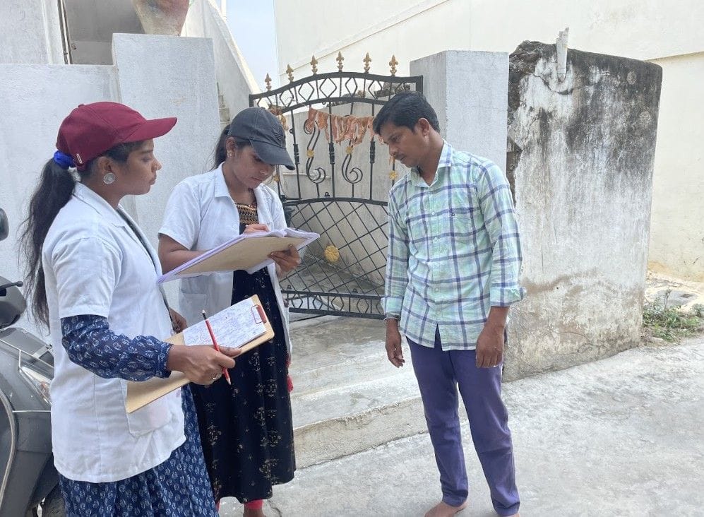 Healthcare workers conducting door-to-door survey and data collection while interacting with a resident in a community setting