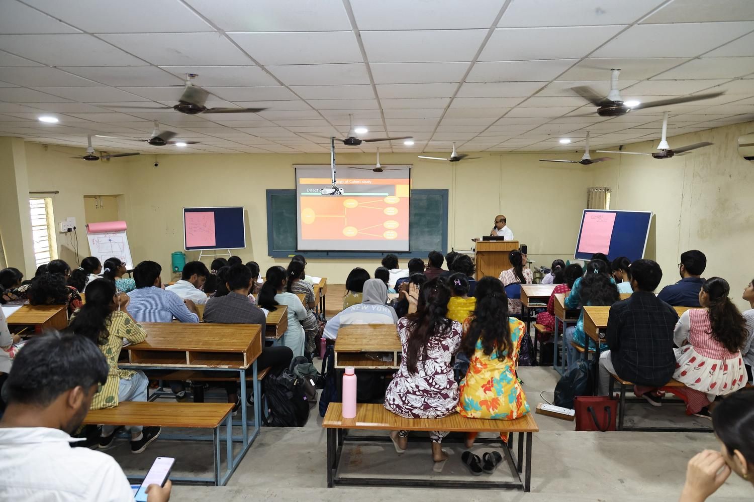 Medical lecture in a classroom with students seated and a speaker presenting slides