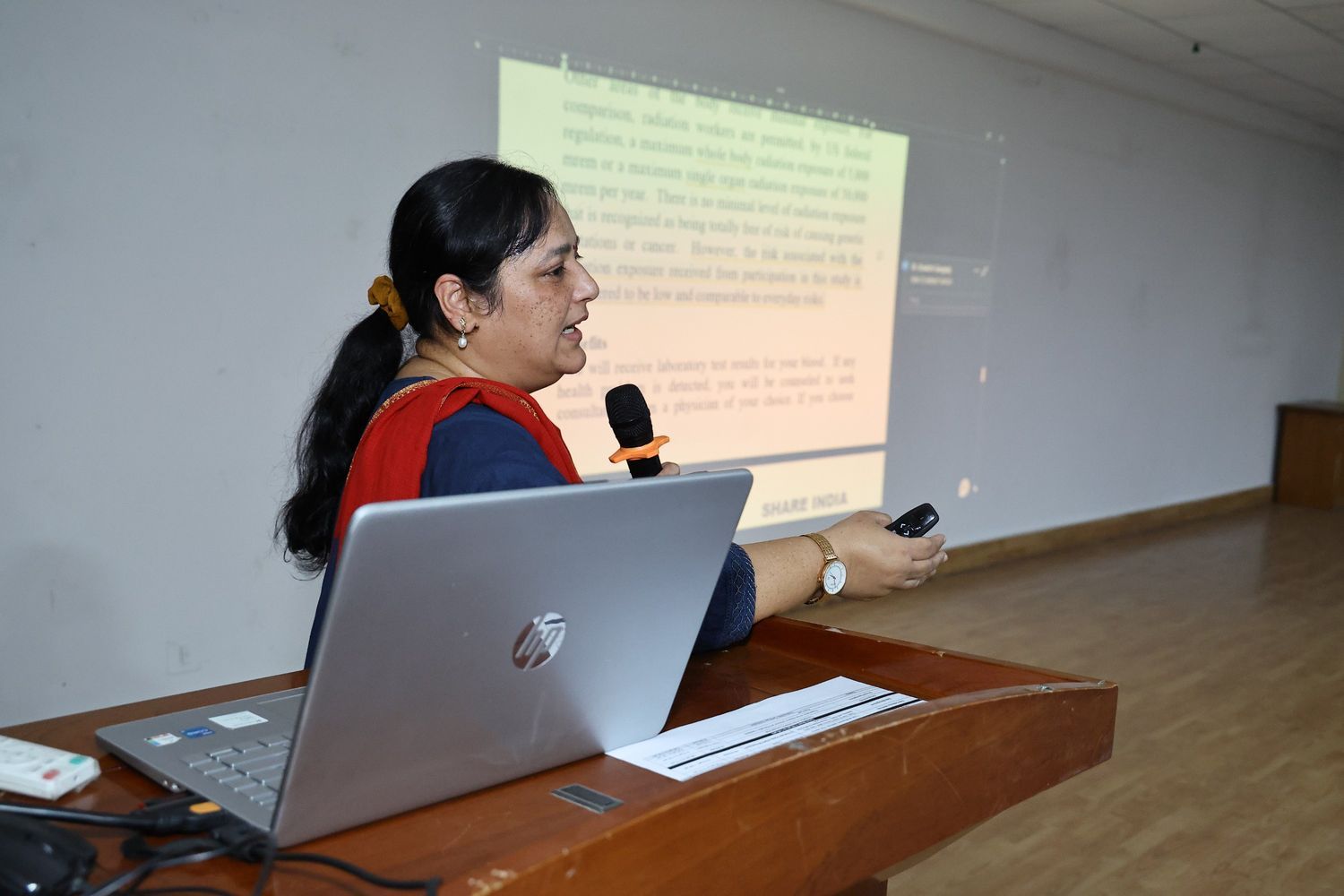 Medical lecture in a classroom with students seated and a speaker presenting slides
