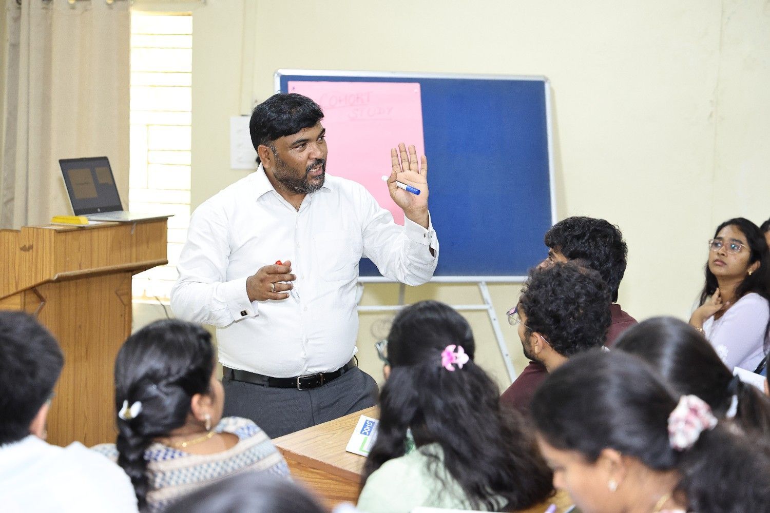 Medical lecture in a classroom with students seated and a speaker presenting slides